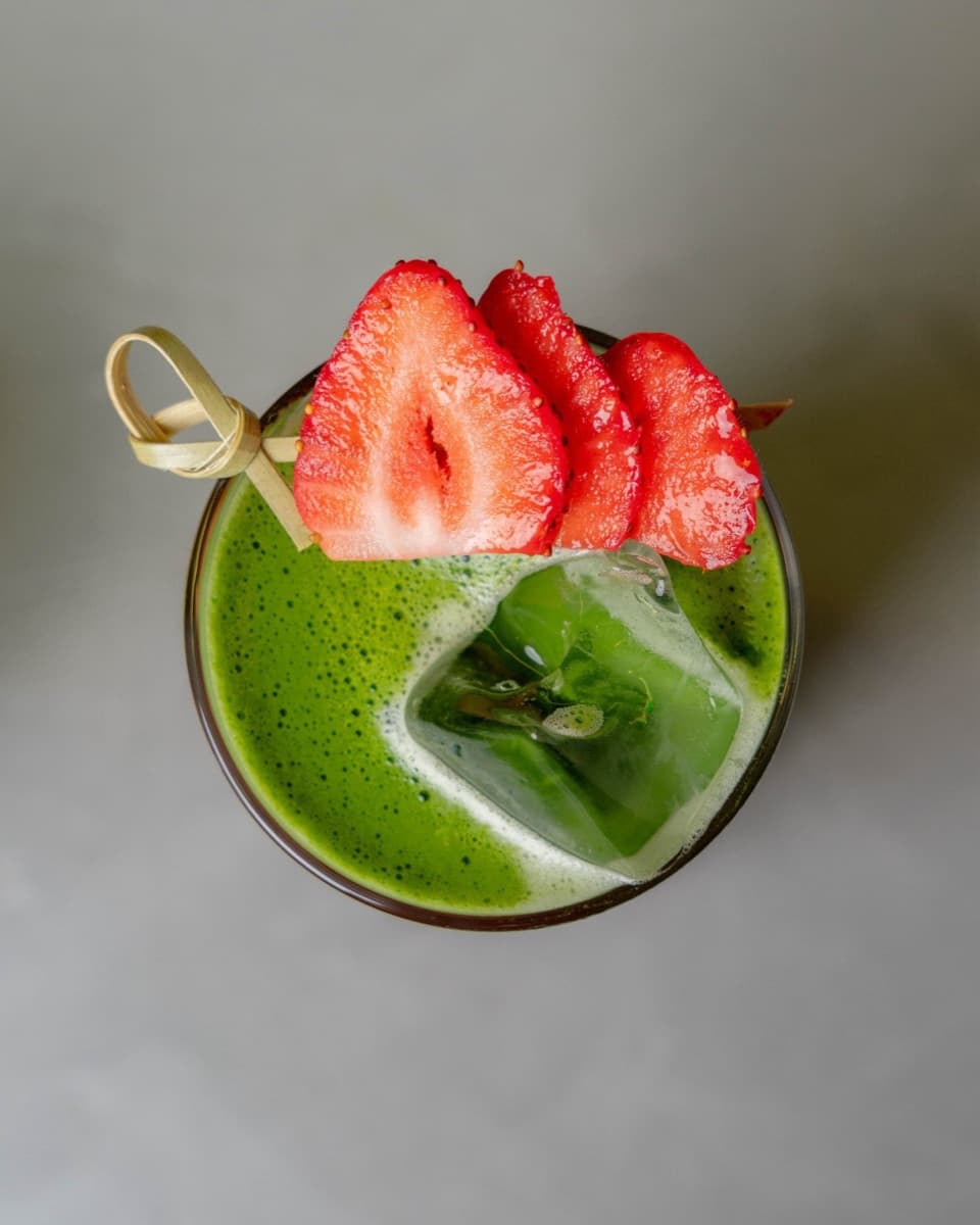 An iced matcha drink garnished with sliced strawberries, shot from above