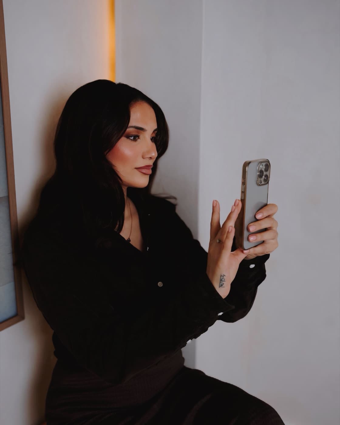 Amalin of Aria Socials sitting against a warm plaster wall, filming on her phone